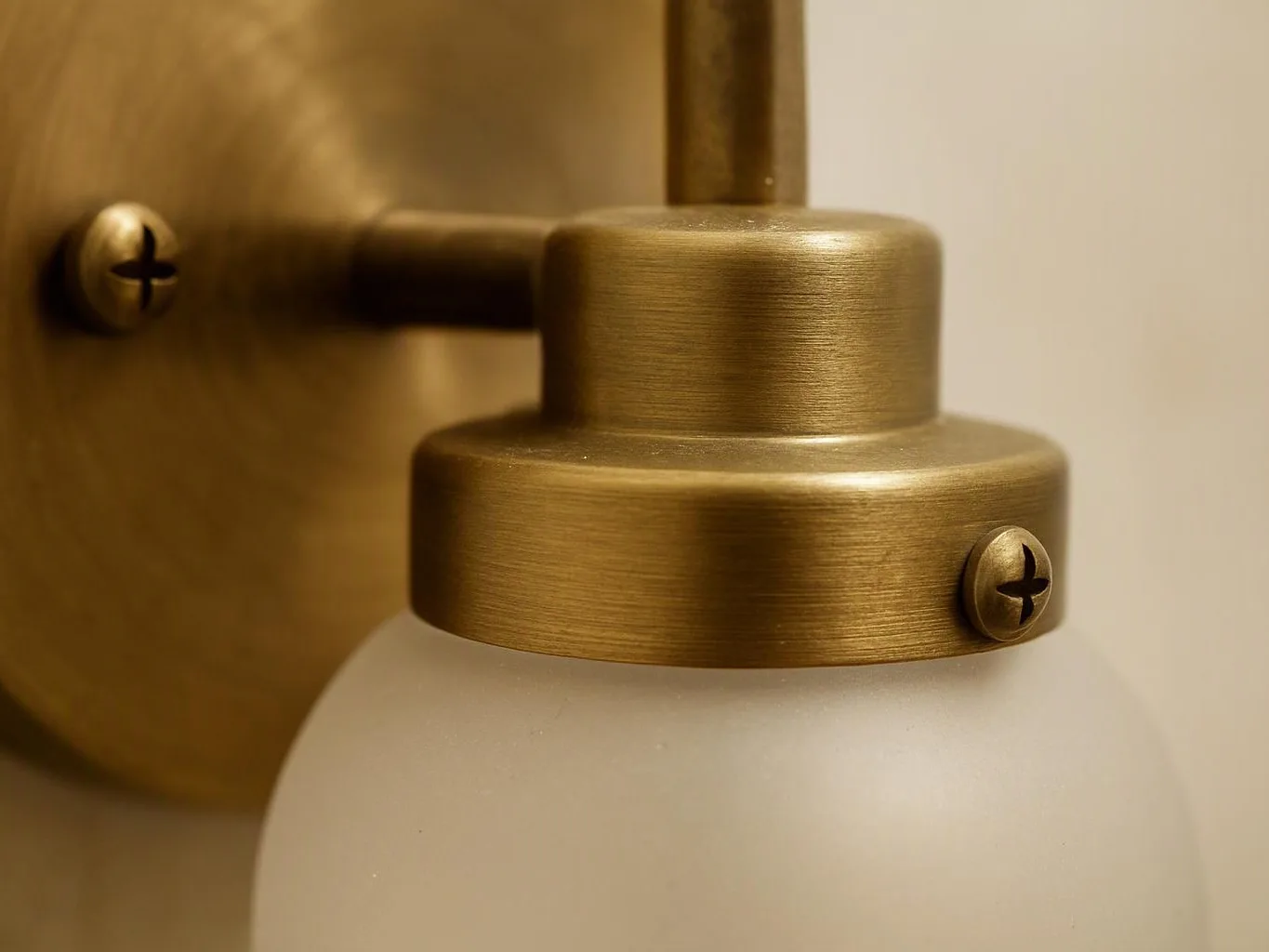 Close-up of a brass wall light with a frosted glass shade against a plain wall