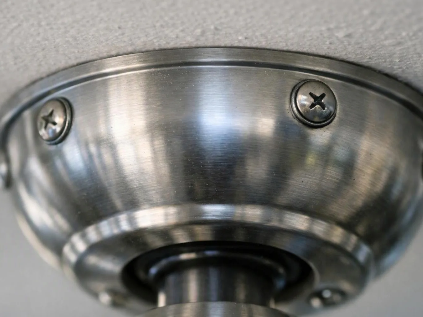 Close-up of a brushed metal ceiling light fixture with two visible screws against a textured ceiling