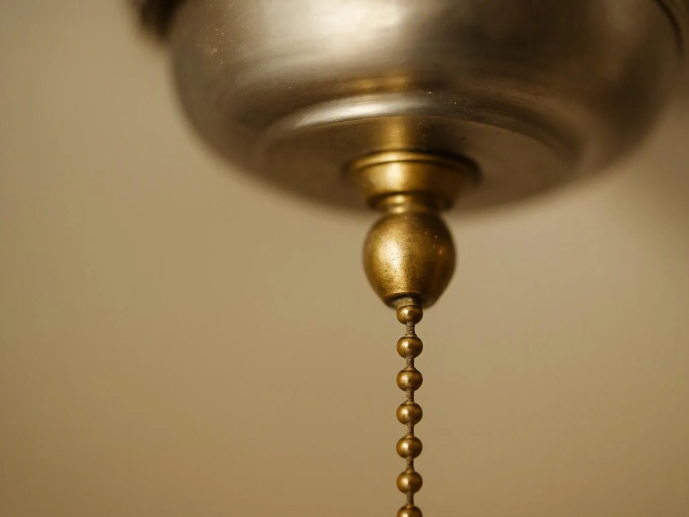A close-up shows a brass ceiling fan pull chain hanging against a plain beige wall