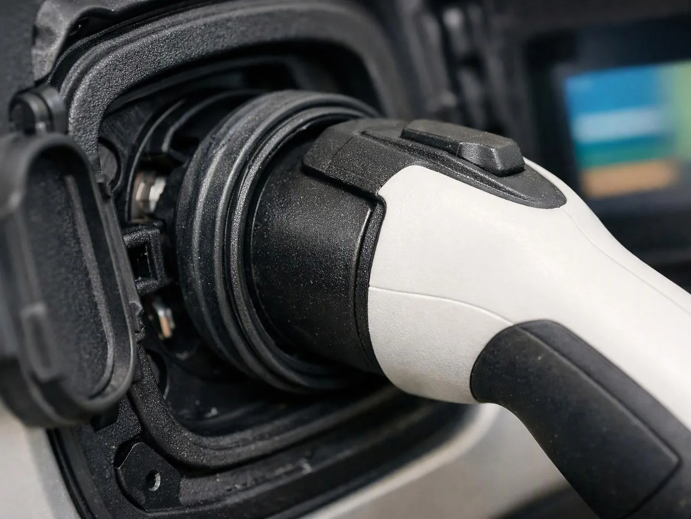 A close-up shows a white and black electric vehicle charging plug inserted into a charging port